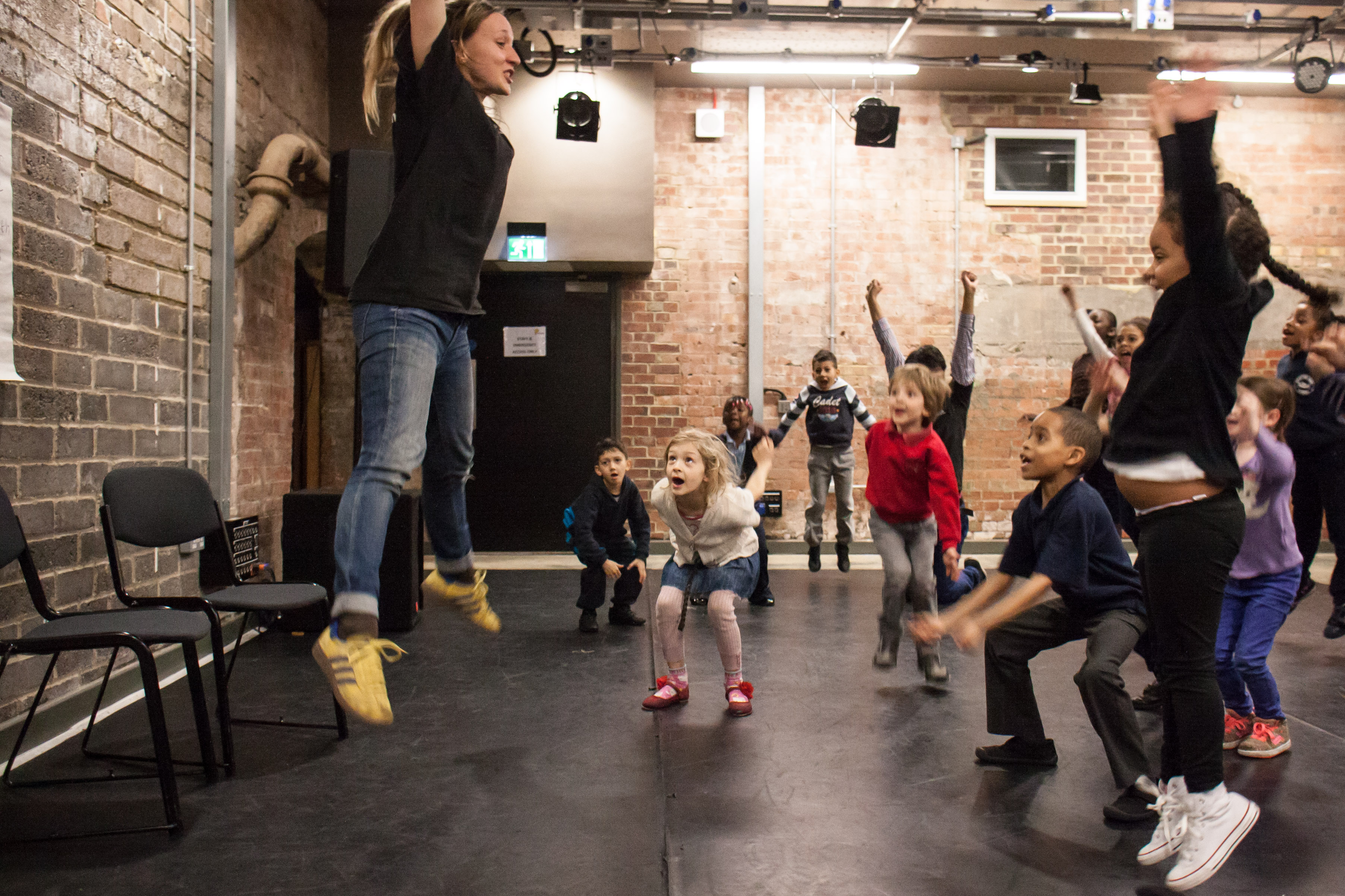 Woman at the front of the room jumping while children try to follow.