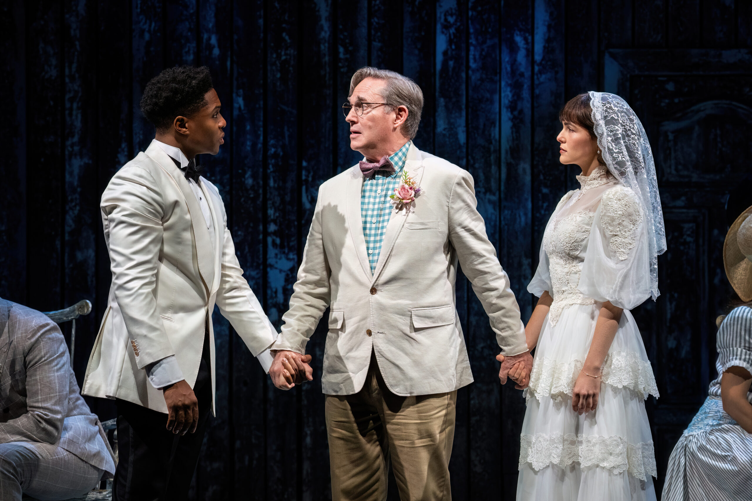 Three characters on stage holding hands