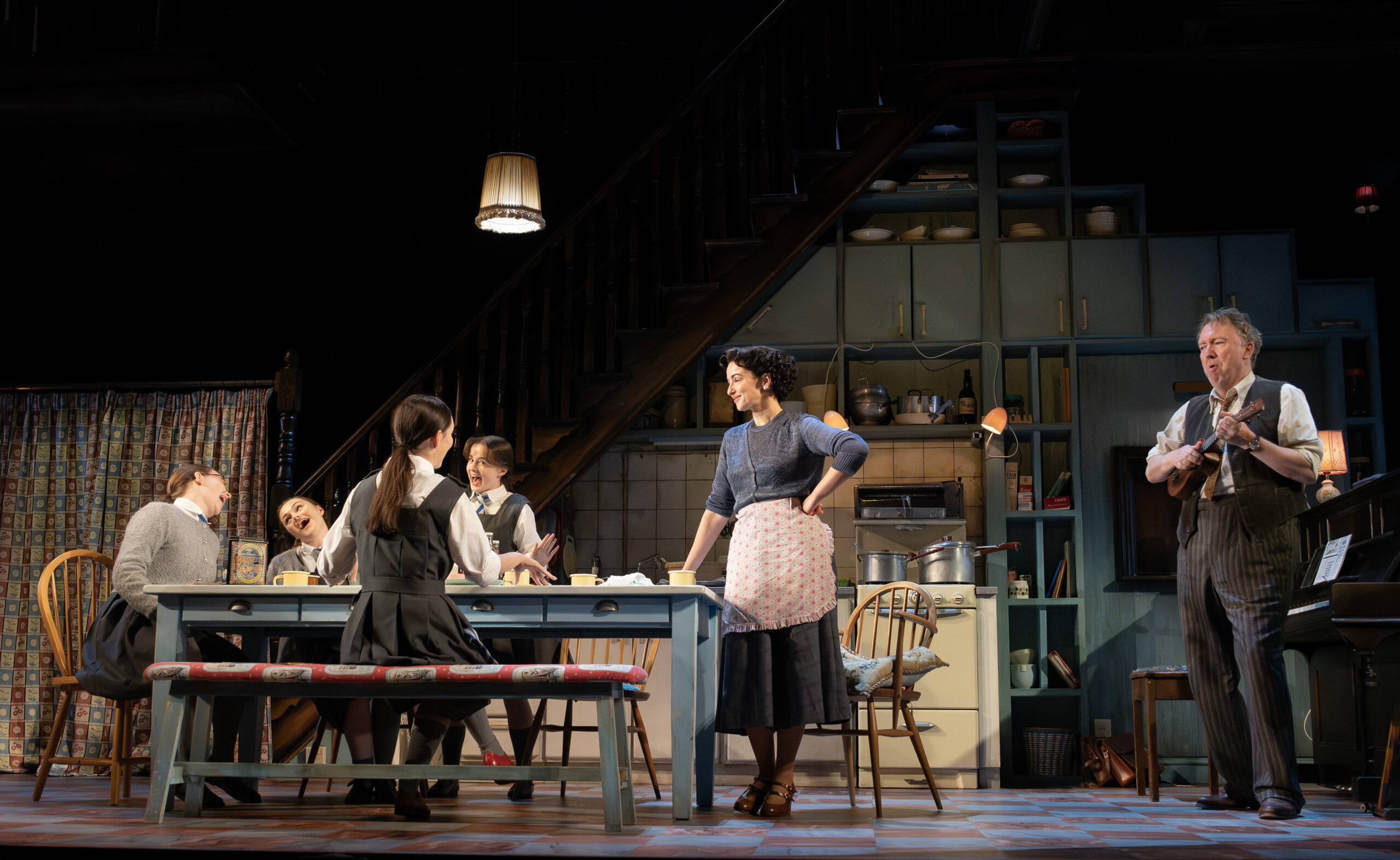 5 characters gathered around a table with a character playing the ukulele stage right