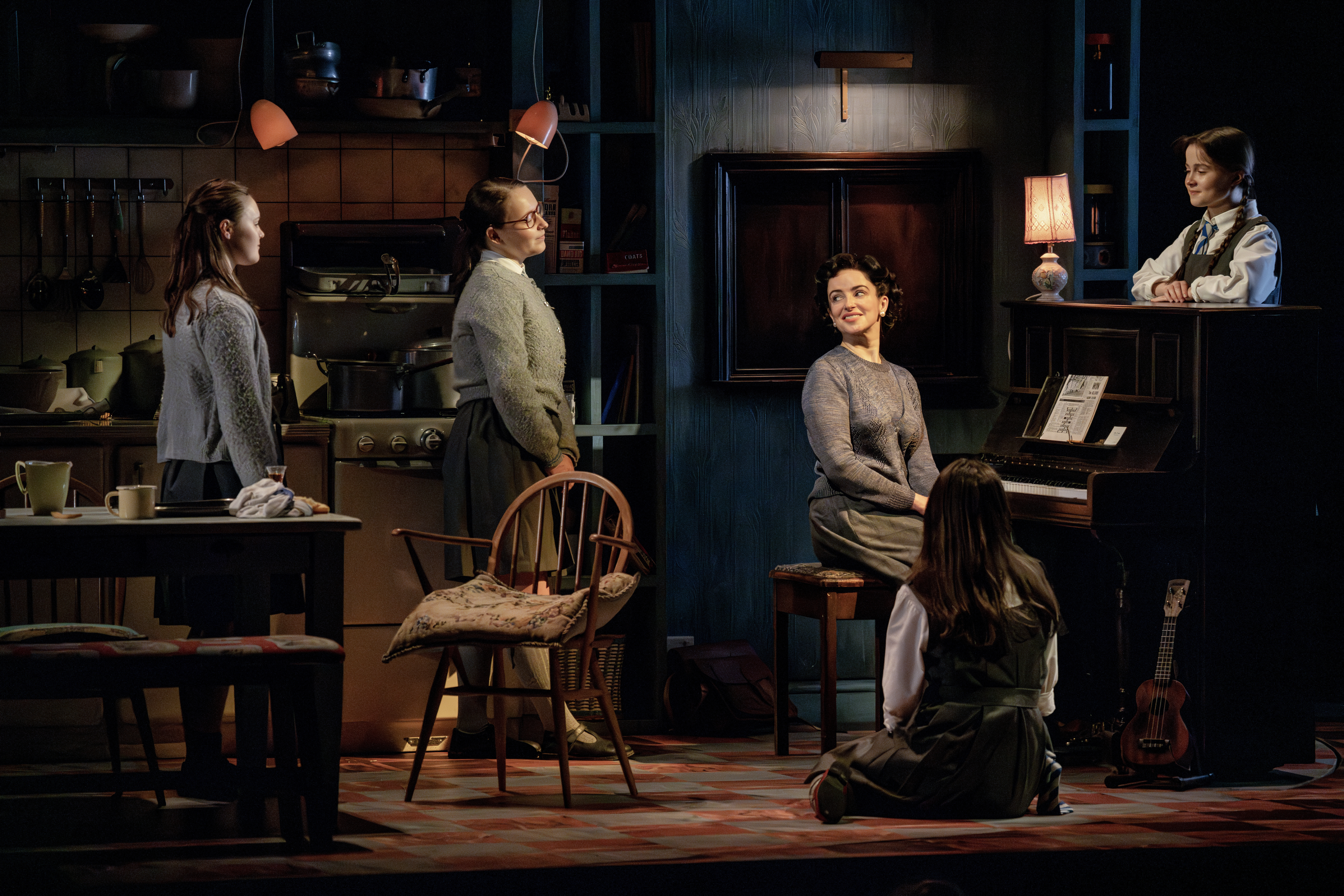 Four characters gathered around a piano with one character sitting at the piano bench looking at the other four. 