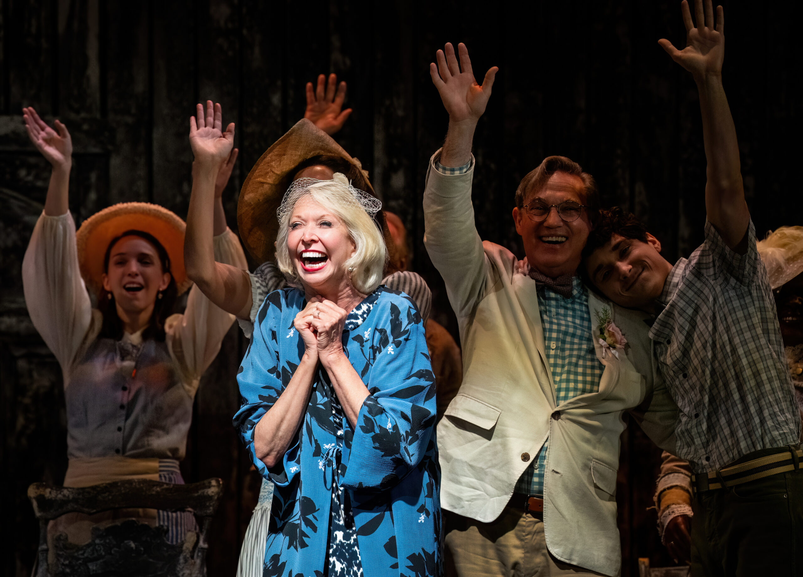A character smiling under a spotlight with four characters behind with their hands raised