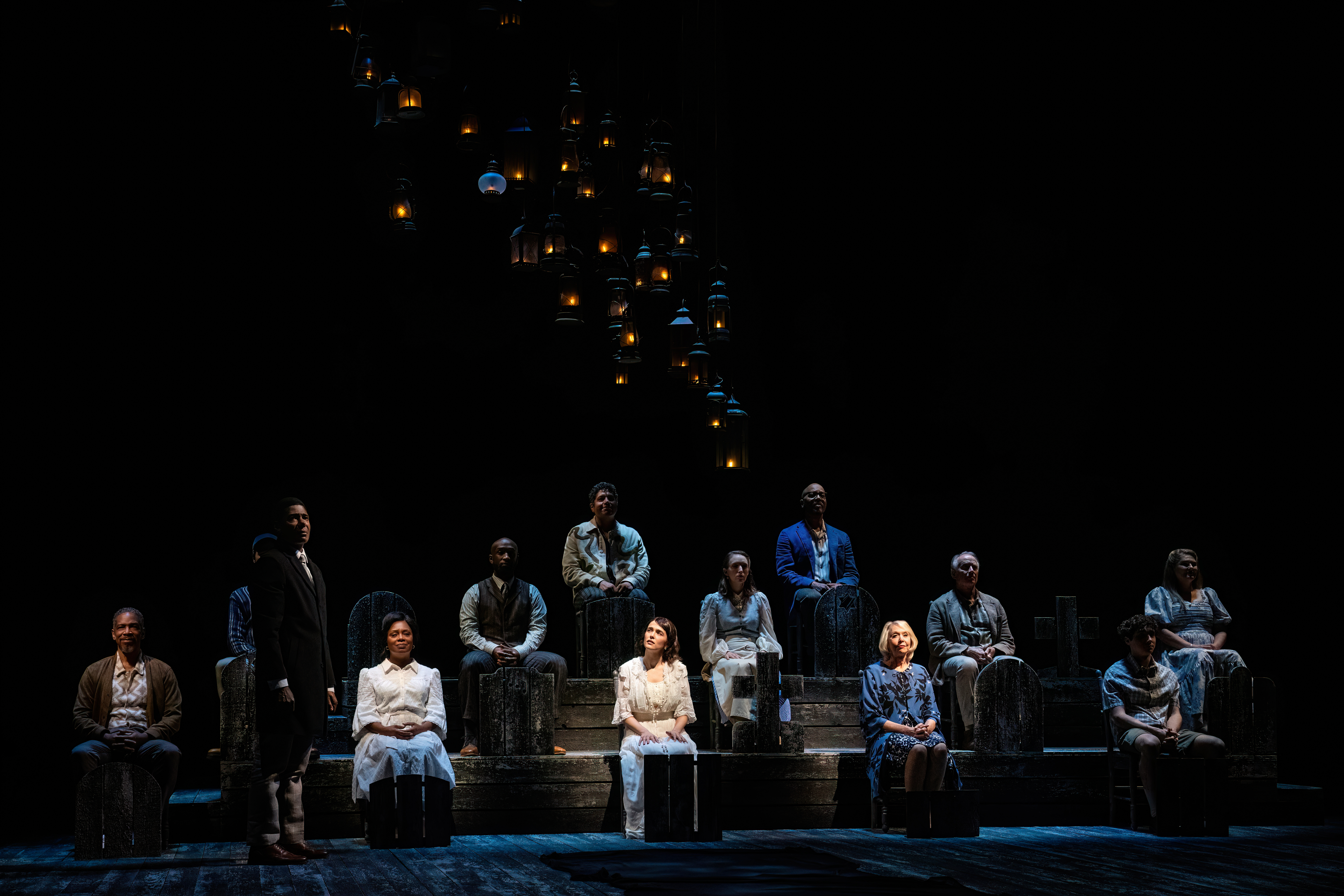 Cast sitting on risers under dim lighting