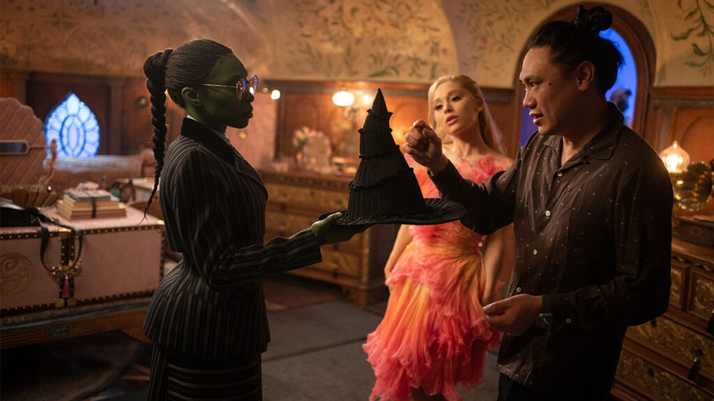 Cynthia Erivo (as Elphaba) and Ariana Grande (as Glinda) with Director Jon M. Chu on the set of WICKED. Photo by Giles Keyte/Universal Pictures.