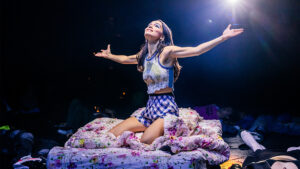 Rachel Zegler pictured sitting on a bed in Romeo + Juliet. Photo by Matthew Murphy and Evan Zimmerman.